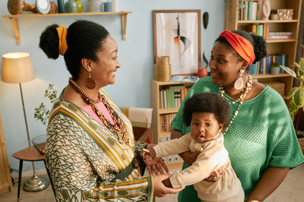 Two Black Women Chatting while Holding Baby at Home